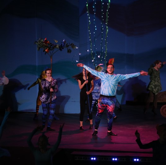 A scene of sea creatures, puppeted by actors on a stage in various colorful costumes