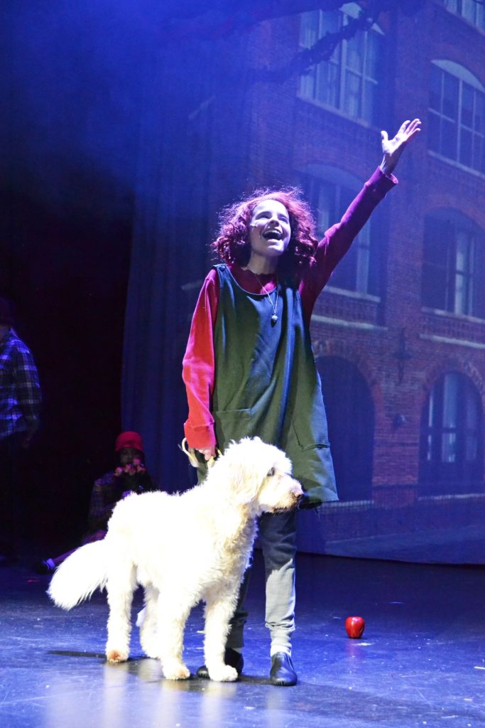 Annie singing a solo with a fluffy dog standing next to her
