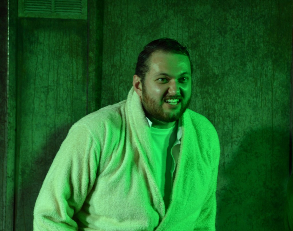 A man baring his teeth menacingly in a bathrobe, under spooky lighting