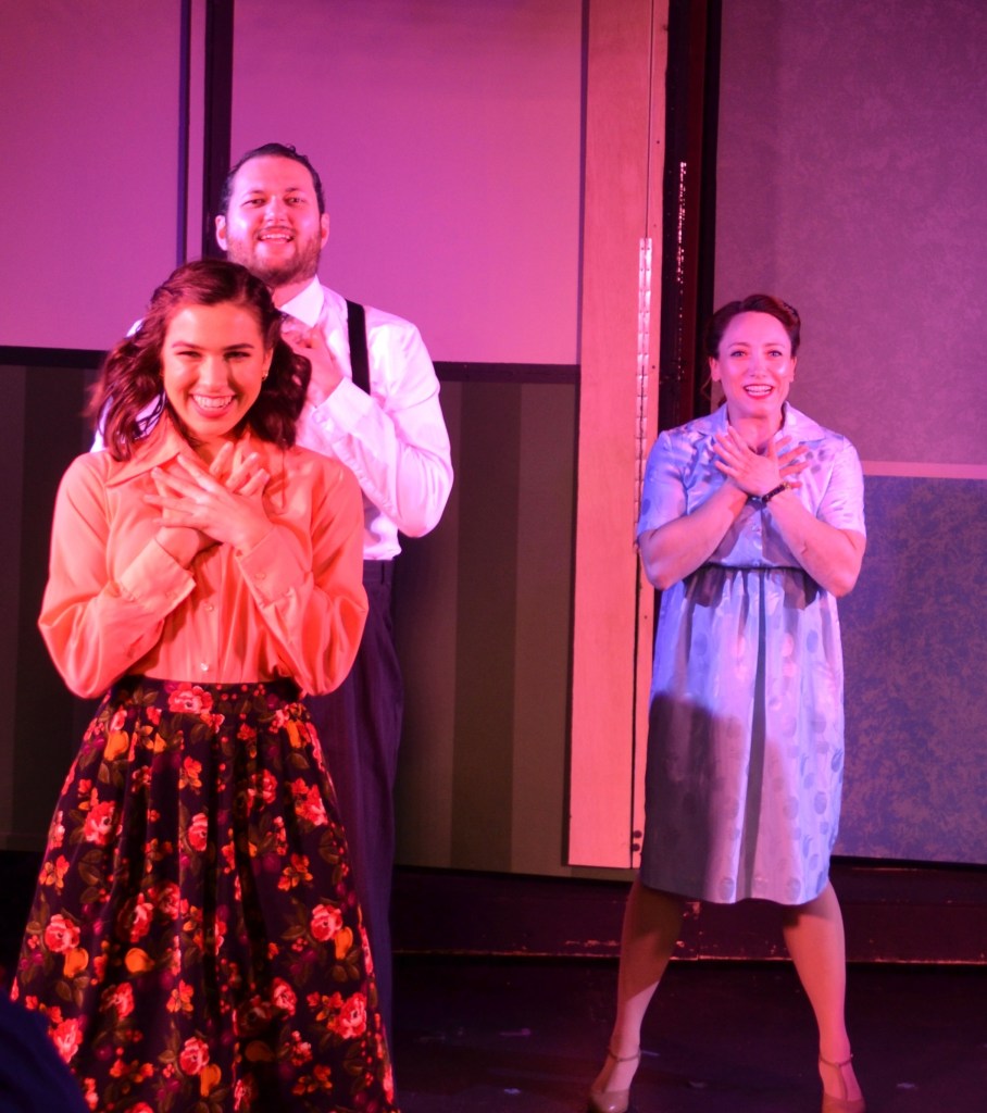Three performers holding their hands to their chests mid dance move