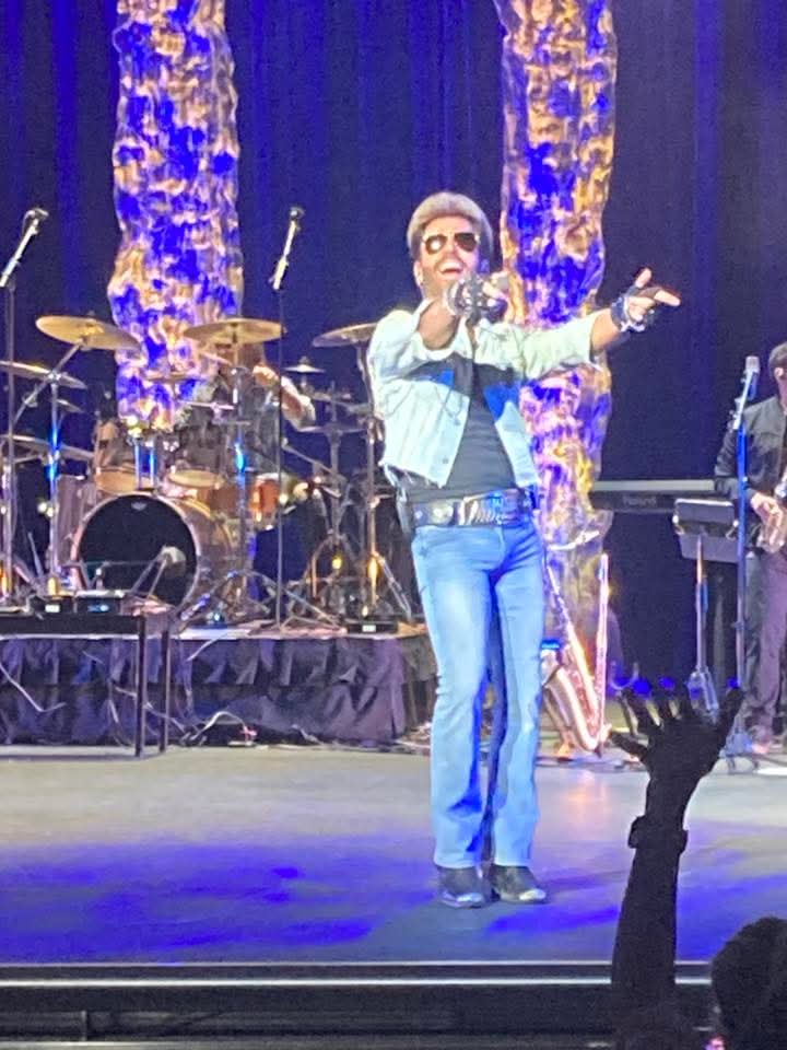 Performer dressed as George Michael singing out the crowd with an outstretched hand